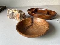 One polished side of petrified wood displaying natural patterns alongside two olive wood bowls on a flat surface.