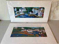 Two unframed prints by Gina Ferrell of Polperro, England, with mats, leaning against a wall on a table