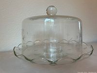 Clear glass cake stand with wavy scalloped edges shown empty, side angle view.