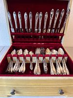 Wooden box containing set of knives, spoons, forks with red velvet lining, arranged in rows inside the box.