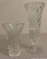 Photo of two vases side by side showing size and cut patterns, smaller one is Waterford crystal with scalloped edge and intricate cuts, taller one is clear cut glass with pedestal base.