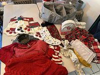 Photo showing the cast steel tree stand, nine assorted Christmas stockings, two fabric tree skirts, two tablecloths, disposable paper plates, festive ribbons, and a gray fabric organizer with ripped handle all arranged on a table.