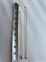 Two necklaces laid side by side next to a measuring tape showing approx. 8 inches chain length to pendant.
