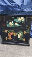 Full front view of black lacquered cabinet with painted lotus and foliage motif.