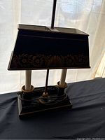 Front and side view of the antique desk lamp showing the decorative shade with floral and shell pattern, dual candle style lights, and the rectangular base.