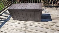 Front view of closed brown plastic outdoor deck box on wooden deck.