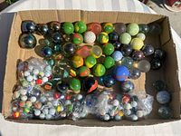 Box of marbles showing assorted sizes and colors, includes loose and plastic bag groups