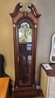 Full view of tall wooden case grandfather clock showing swan neck pediment, glass front door; mechanical clock inside