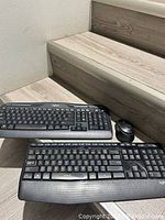 Two Logitech keyboards and one Logitech wireless mouse with USB dongle on wooden stairs.