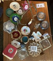 Overview of assortment of ashtrays, candles in glass and ceramic holders, small figurines, and decorative items on wooden table.