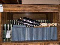 Shelf with stacked blue hardcover Shakespeare books and green spined Funk & Wagnalls encyclopedias with additional black and decorative bound books on top
