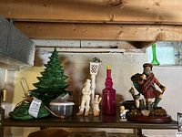 Wide view of the ceramic Christmas tree, Scottish Santa figurine, two white decorative figurines, magenta bottle, and small figurine on a shelf.
