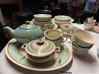 Full display of china pieces including plates, side plates, teacups stacked, sugar bowl with lid and teapot arranged on a table.