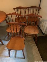 Five wooden dining chairs including four matching and one single chair, placed near a wooden dining table on floor with linoleum tiles.