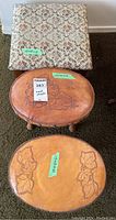 Three footstools shown together, two oval leather embossed with leaf motif, one square fabric upholstered with floral pattern