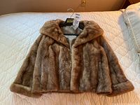 Front view of the brown fur jacket spread on bed with collar and button details visible.