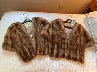 Top view of two brown fur stoles laid side by side on a white quilt, showing length and texture