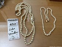 Two pearl necklaces laid out on wooden surface, showing length and clasps.