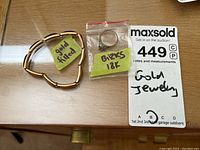 Photo of an 18K Birks gold ring inside a small plastic bag and a gold filled expandable bracelet laid next to a MaxSold auction card.