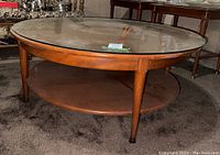 Glass-topped round coffee table front and side view showing wood base, tapered legs, and lower wooden shelf.