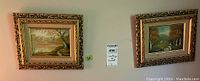 Two framed landscape paintings hung on wall showing matching ornate carved gold-tone frames.