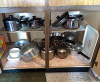 Kitchen cabinet shelf with assortment of pots, pans, mixing bowls, and ceramic serving platter