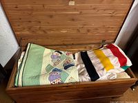 Open cedar chest showing folded patchwork quilt and striped wool blanket inside