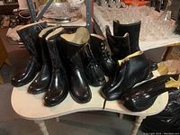 Six pairs of men's industrial rubber rain boots of various styles and shapes on a white table surface in a basement setting