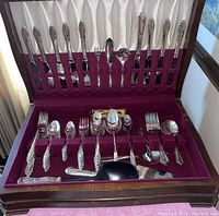 Full view of silver plated flatware set neatly arranged in a lined box cabinet with purple velvet and white satin lining.