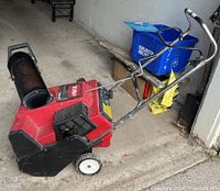 Photo of the snow blower showing the left side with the chute and wheels, giving a view of the overall shape and size.