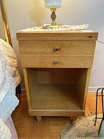 Front view of one nightstand with two drawers and open shelf, showing top surface with marks and a lamp on top.