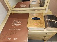 Golden Leaves from Canada's Past book, Oxford Dictionary, and Vitology book on a dresser with mirror.