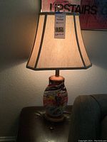 Lamp turned on showing illumination and lampshade details, including a tag with auction info.