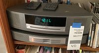 Stacked Bose Wave Music System (top) and Wave Music System Multi-CD Changer (bottom) with two remotes on top, digital clock display showing time