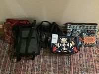 Full lot showing six purses and bags lined up on patterned rug, includes patchwork Coach purse, black handbag, backpack, and patterned clutches.