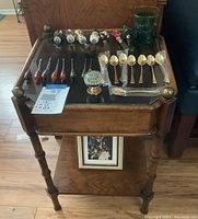 Straight on view of wooden display table with glass top holding holiday-themed forks, knives, small forks, gold spoons, a green glass container, and decorative knob visible.