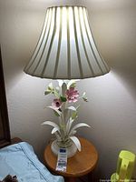 Illuminated metal floral lamp with cream fabric shade on a round wooden stool.