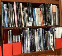 Two-shelf bookcase filled with glass art books and auction catalogs. Red magazine holders flank the collection on lower shelf.