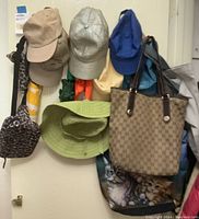 Photo showing hats hung on hooks including various caps and bucket hats, along with two tote bags, one having a kitten print.