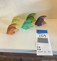 Five glass fish arranged in a row on a white surface.