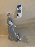 Front view of the Lladro porcelain statue showing the woman holding the bird with dog at her feet, attached to a clear textured glass base.