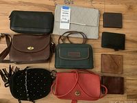 Full view of 9 assorted purses and wallets arranged on wood floor showing different styles and colors.