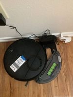 Robotic vacuum with dustbin compartment and docking station charger on wooden floor.