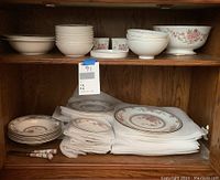 Wood cabinet shelves showing Royal Doulton Canton china set arranged with bowls, plates, and cups. Cloth or paper padding beneath plates.
