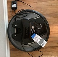 Black Shark Ion robotic vacuum with charging dock and power adapter on wooden floor.