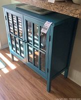 Front-side view of teal wooden cabinet with glass doors, showing structure and legs.