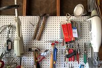 Photo showing pegboard with various hand tools including hammers, pliers, snips, and a pack of coping saw blades, handheld vacuum and steam sweeper hung
