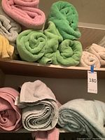 Rolled assorted color towels stacked on a shelf, including pink, green, gray, yellow, beige, and light blue towels.