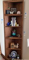 Full view of tall wooden corner shelf with various decorative and office items on shelves.
