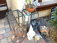 Photo showing two wrought iron tables, metal Texas star, white garden gnome, cat statue holding lantern, dog statue, and tortoise with seashells